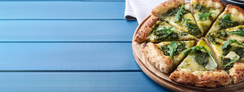 Delicious pizza with pesto, cheese and arugula on blue wooden table, space for text. Banner design - Foto, immagini