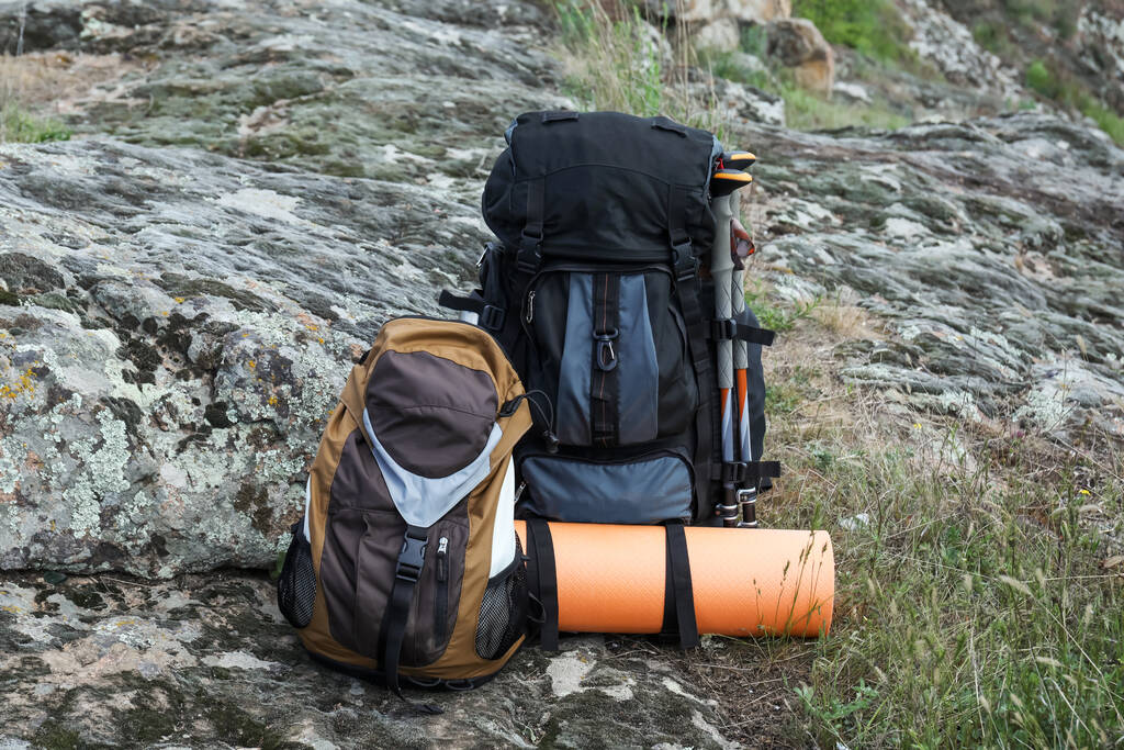 Backpacks with trekking poles and camping mat on rocky hill - Zdjęcie, obraz