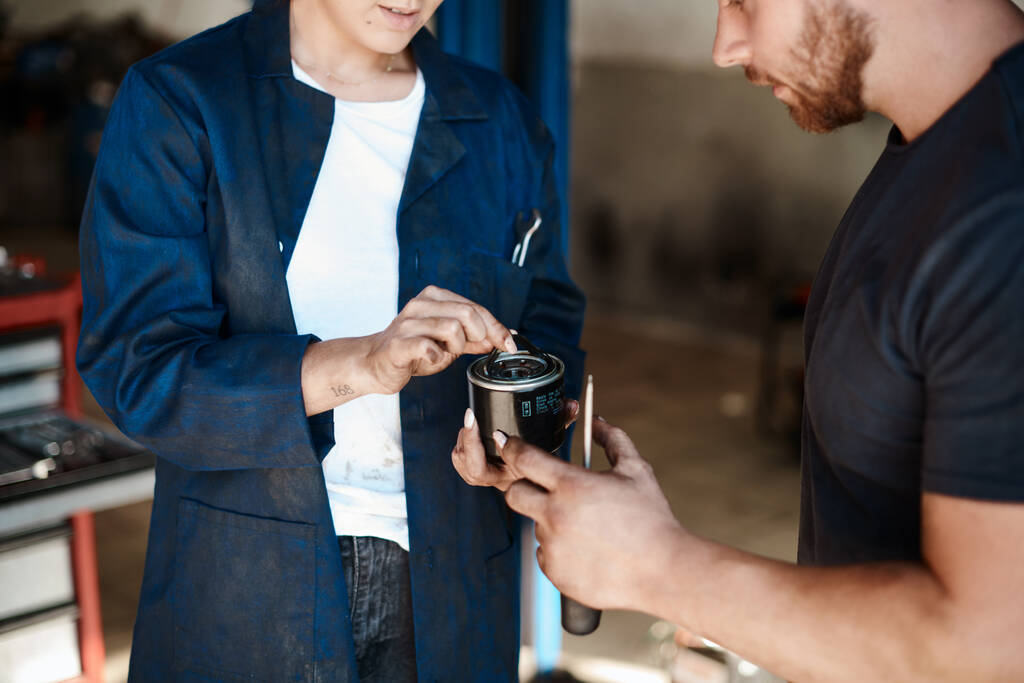 Bueno, tengo que reemplazar esto. Fotografía de dos mecánicos mirando un filtro de combustible mientras trabajan juntos en un taller de reparación de automóviles. - Foto, imagen