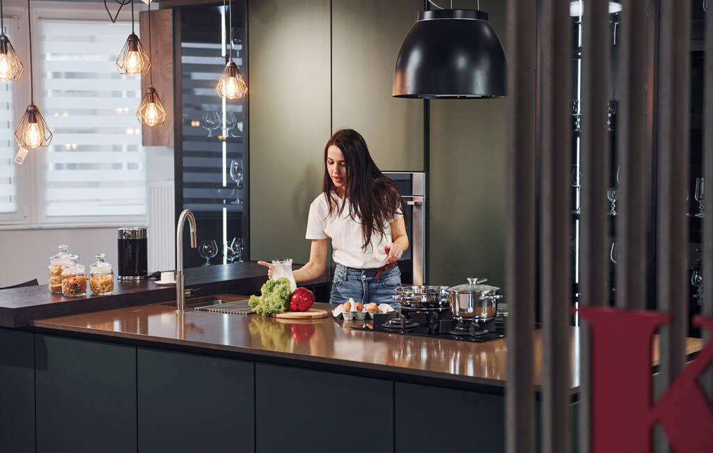 Young beautiful brunette in casual clothes preparing healthy food in kitchen at daytime. - Photo, image