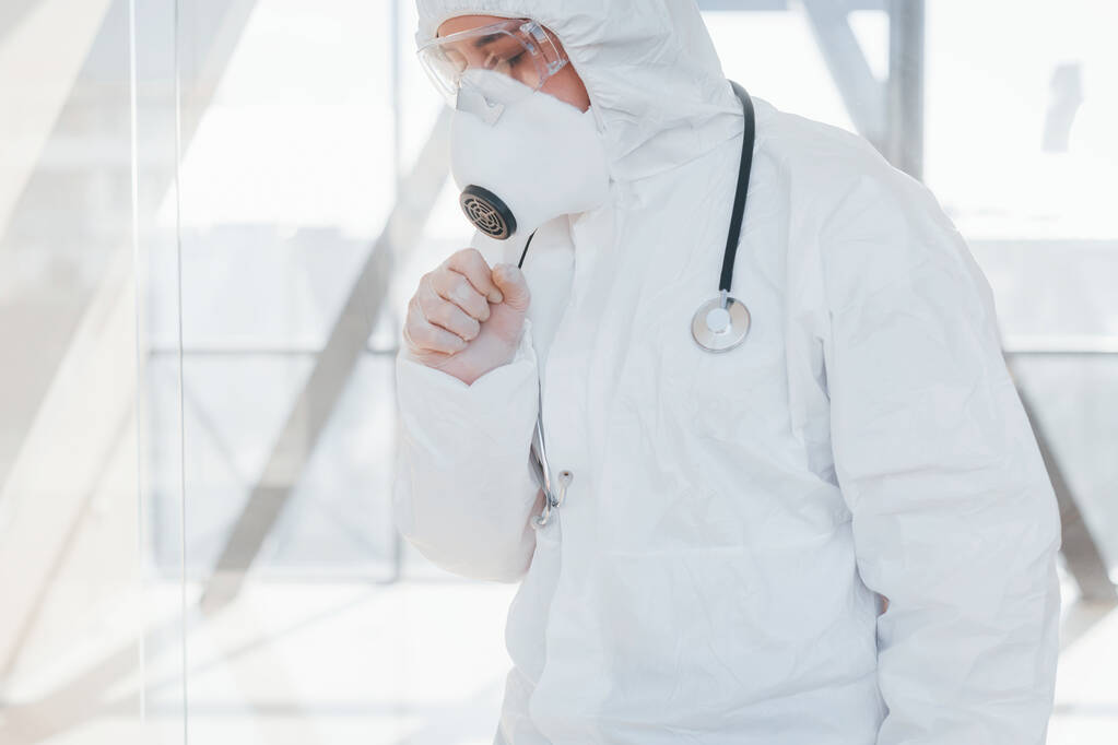 Feels bad and sick. Female doctor scientist in lab coat, defensive eyewear and mask standing indoors. - Foto, immagini
