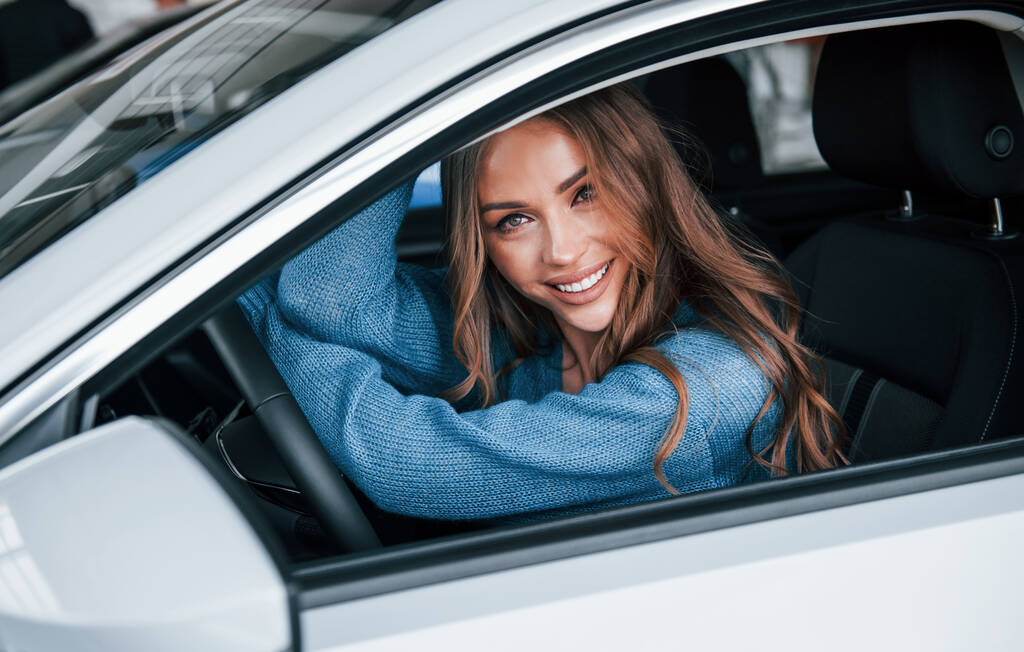 Positive woman in blue shirt sits inside of new brand new car. In auto salon or airport. - Valokuva, kuva