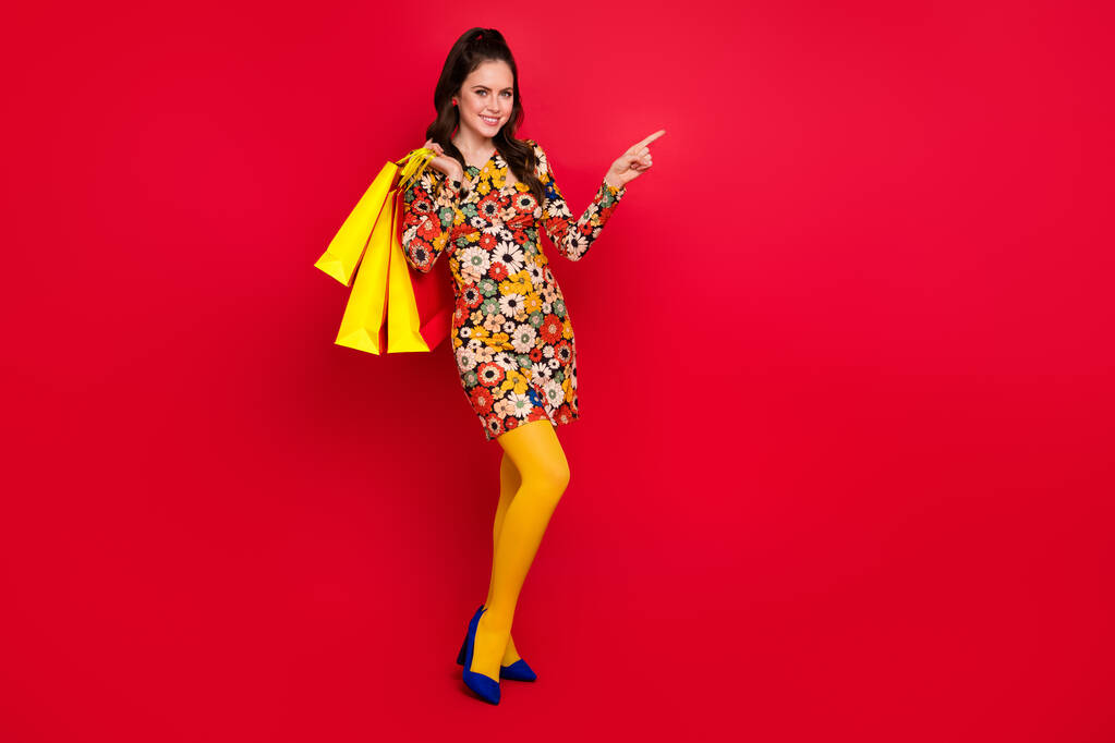 Fotografie okouzlující sladká žena nosit květinový tisk šaty držení nakupující ukazující prázdný prostor izolované červené barvy pozadí - Fotografie, Obrázek