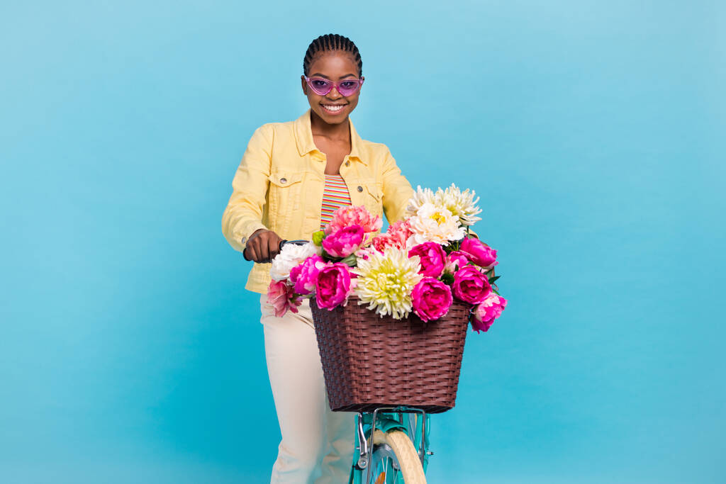 Ritratto di attraente allegra ragazza funky equitazione bici giardino fioritura isolato su sfondo di colore blu brillante - Foto, immagini