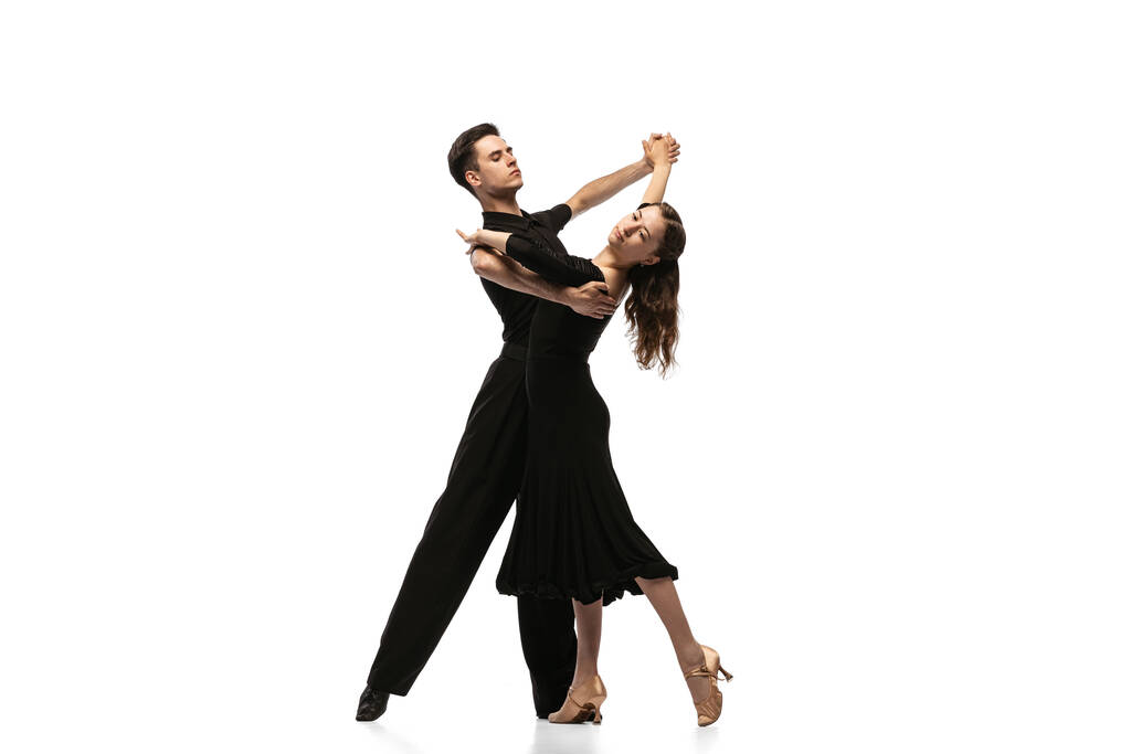 Dos jóvenes bailarines elegantes con trajes de escenario negro bailando bailes de salón aislados sobre fondo blanco. Concepto de arte, belleza, música, estilo. - Foto, Imagen