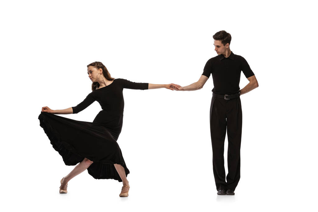 黒の衣装を着た若い感情的なダンサーのダイナミックな肖像は、白い背景に隔離されたボールルームダンスを踊る。芸術、美、音楽、スタイルの概念. - 写真・画像