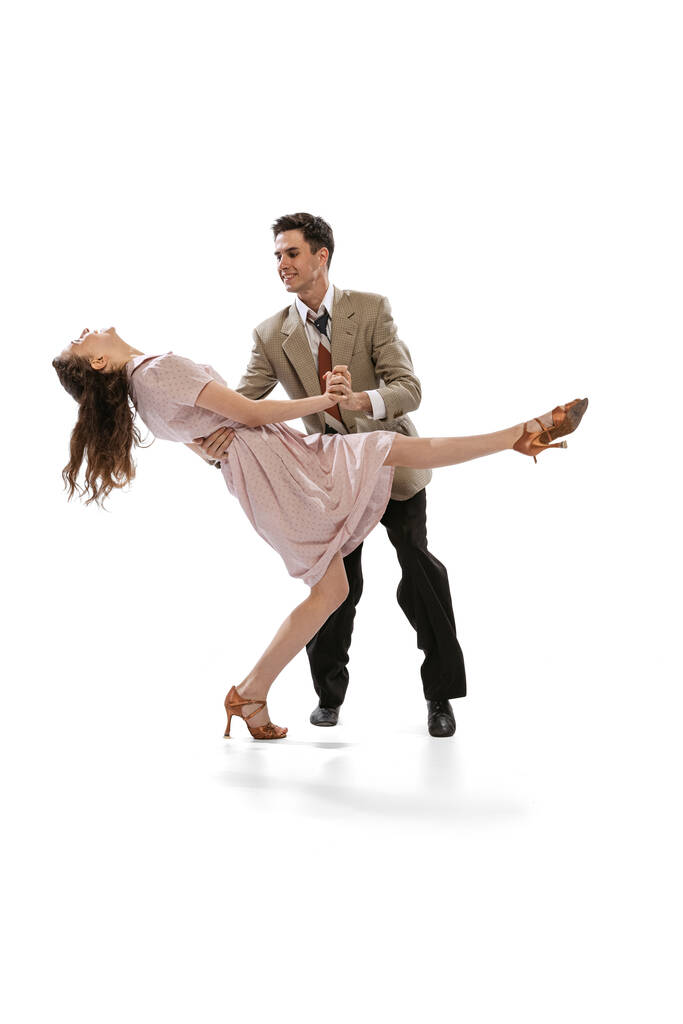 Молодой человек и женщина в винтажных костюмах в стиле ретро танцуют социальный танец на белом фоне. Вечные традиции, стиль и искусство американской моды 1960-х годов - Фото, изображение