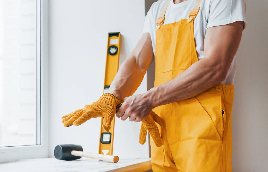 Handyman in yellow uniform preparing for work indoors. House renovation conception. - Фото, изображение