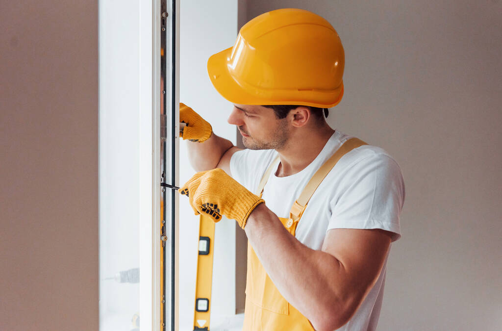 Handyman in yellow uniform installs new window. House renovation conception. - Zdjęcie, obraz