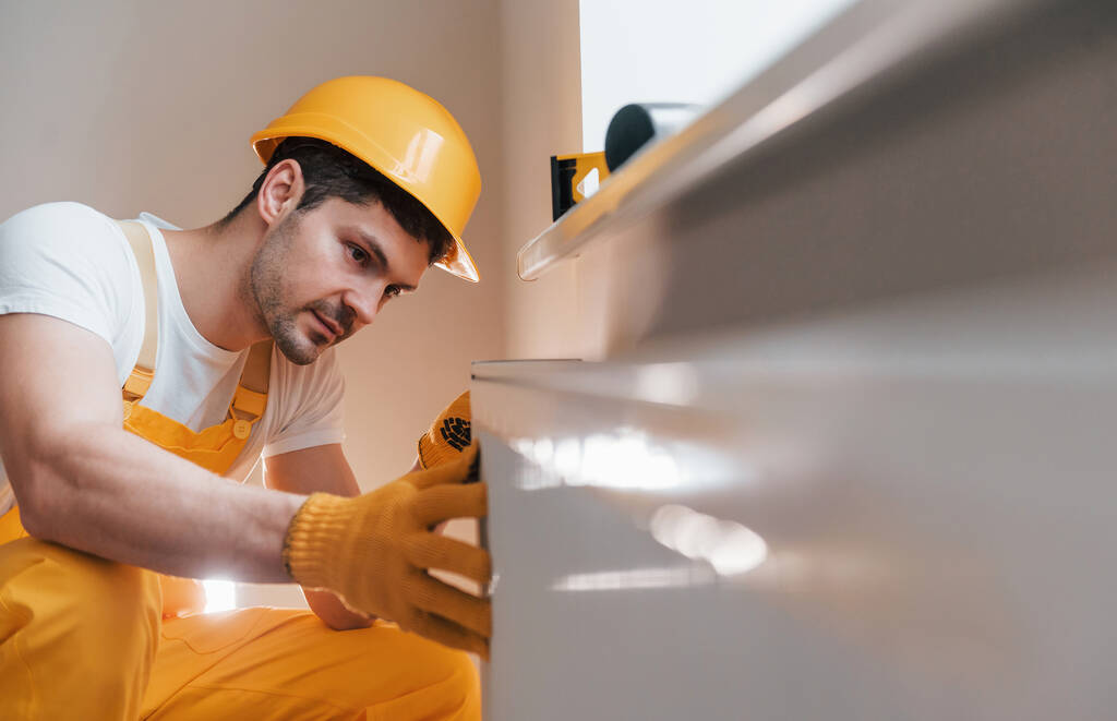 Handyman ve žluté uniformě instaluje novou baterii. Koncepce rekonstrukce domu. - Fotografie, Obrázek
