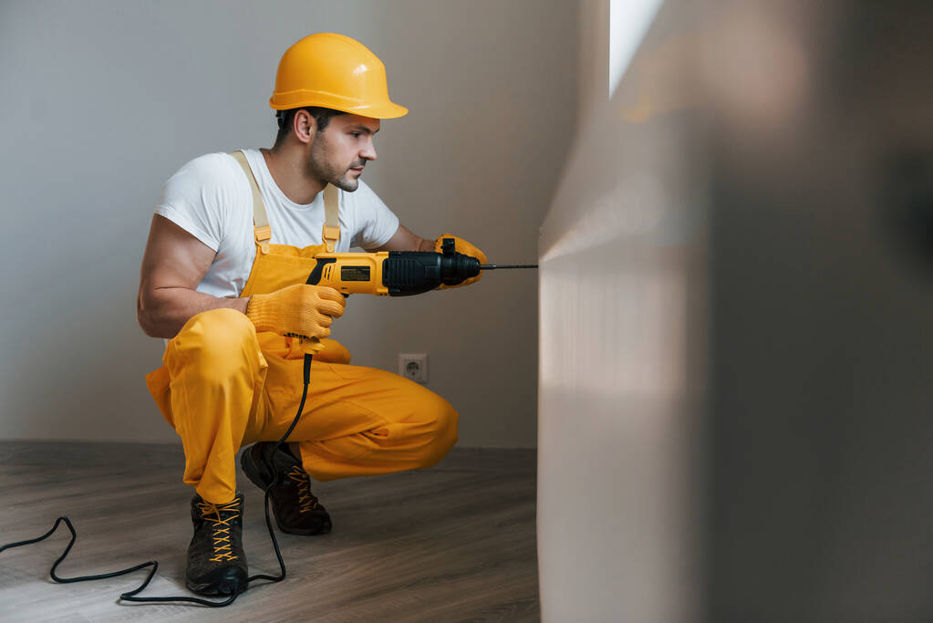 Handyman en uniforme amarillo trabaja con taladro en interiores. Concepto de renovación de casas. - Foto, imagen