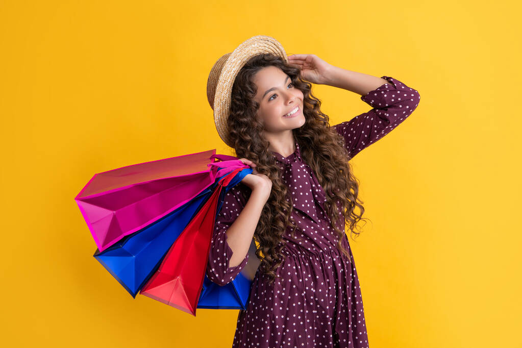 fröhliches Kind mit lockigem Haar hält Einkaufstaschen auf gelbem Hintergrund - Foto, Bild