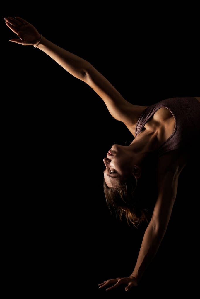 Fit žena cvičit jógu pózuje. Boční osvětlené poloviční silueta dívka dělá cvičení ve studiu proti černému pozadí. - Fotografie, Obrázek