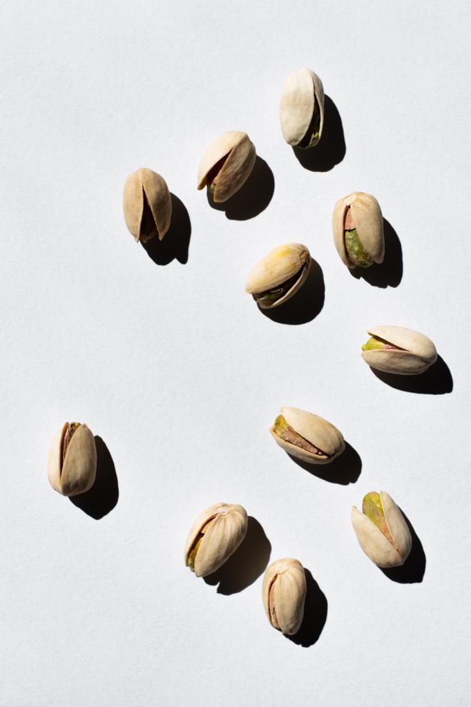 top view of cracked green and salty pistachios on white background  - Foto, Imagen