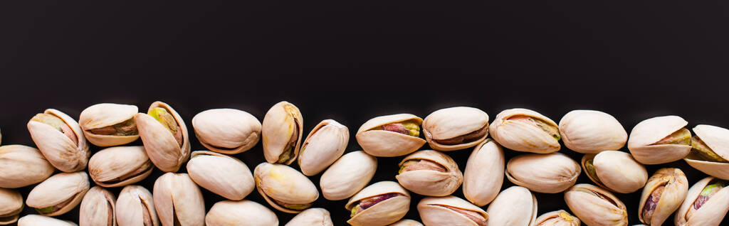 top view of fresh and salty pistachios isolated on black, banner - Фото, изображение