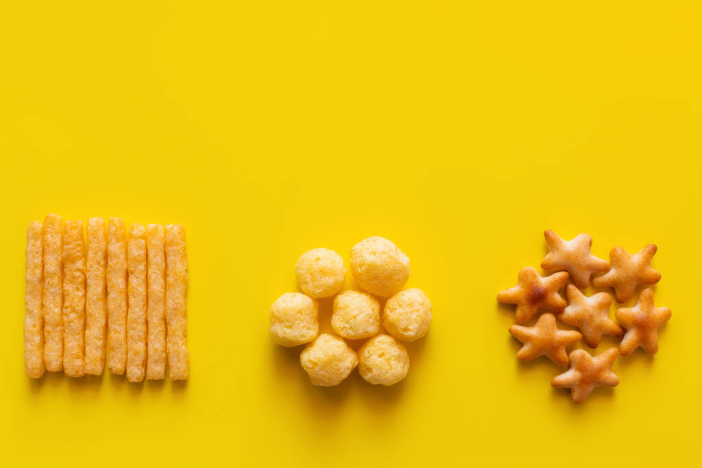 vista superior de saborosas batatas fritas, pops de queijo e bolos forma de estrela biscoitos em amarelo - Foto, Imagem
