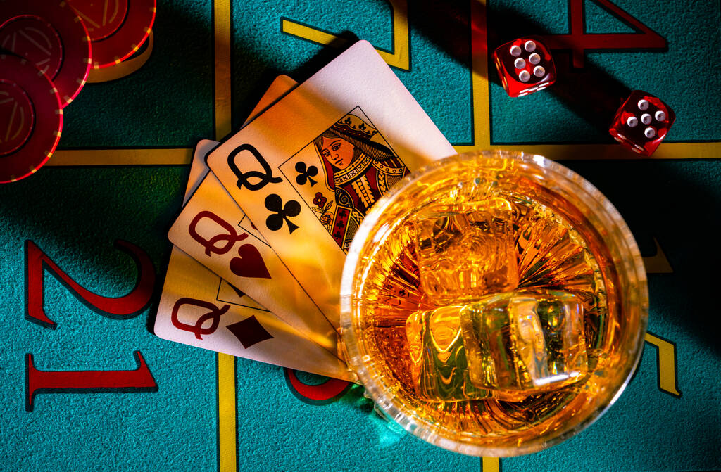 Widok na stół do gier w kasynie ze szklankami whisky i zestawem trzech pań. Zamknij ciemny stół pokerowy z alkoholem, kartami, kostkami i żetonami w kasynie. Zakłady kasynowe. - Zdjęcie, obraz