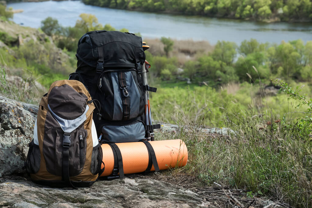 Backpacks with trekking poles and camping mat on rocky hill, space for text - Fotoğraf, Görsel