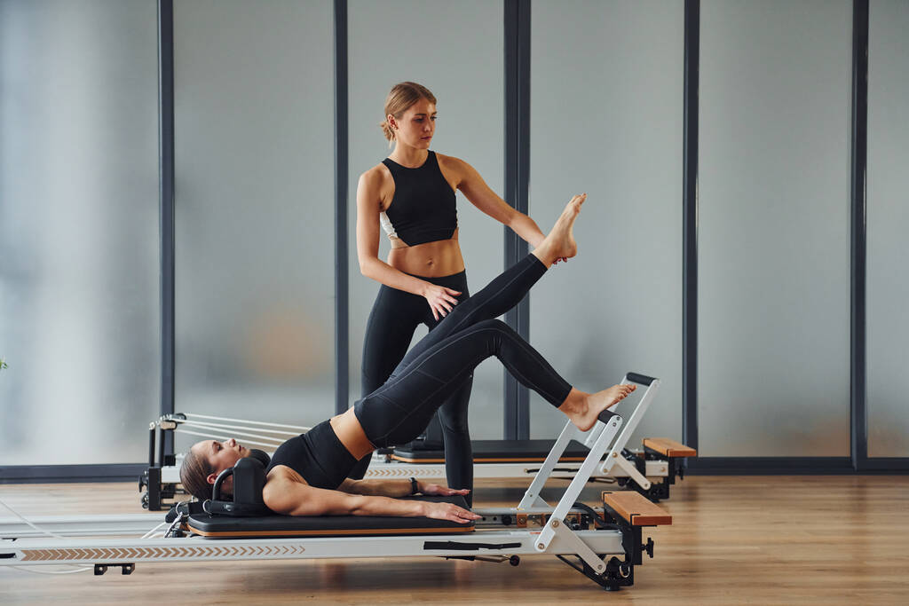 Trainer hilft Mädchen. Zwei Frauen in sportlicher Kleidung und mit schlanken Körpern machen gemeinsam Fitness-Yoga-Tag. - Foto, Bild
