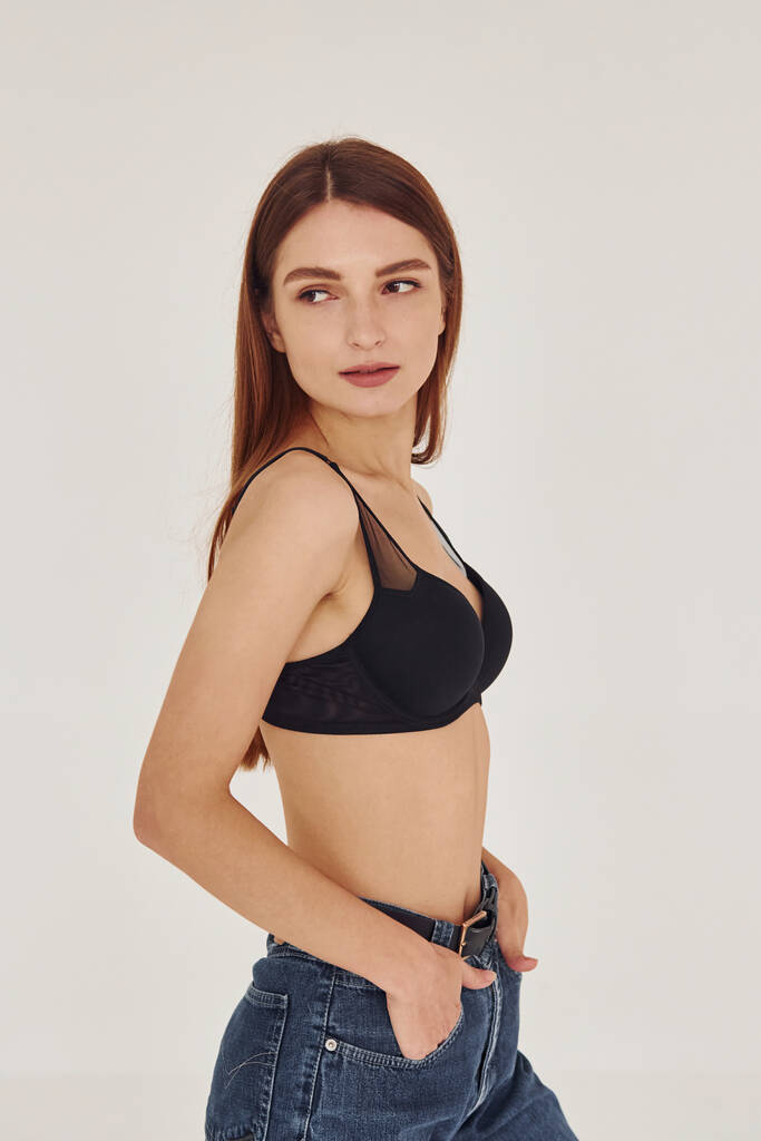 Young woman in jeans and bra indoors. White background. - Photo, Image