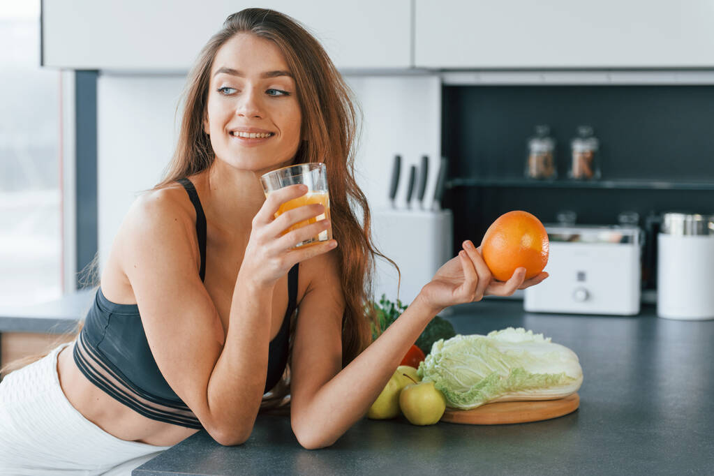 With fresh orange juice. Young european woman is indoors at kitchen indoors with healthy food. - Φωτογραφία, εικόνα