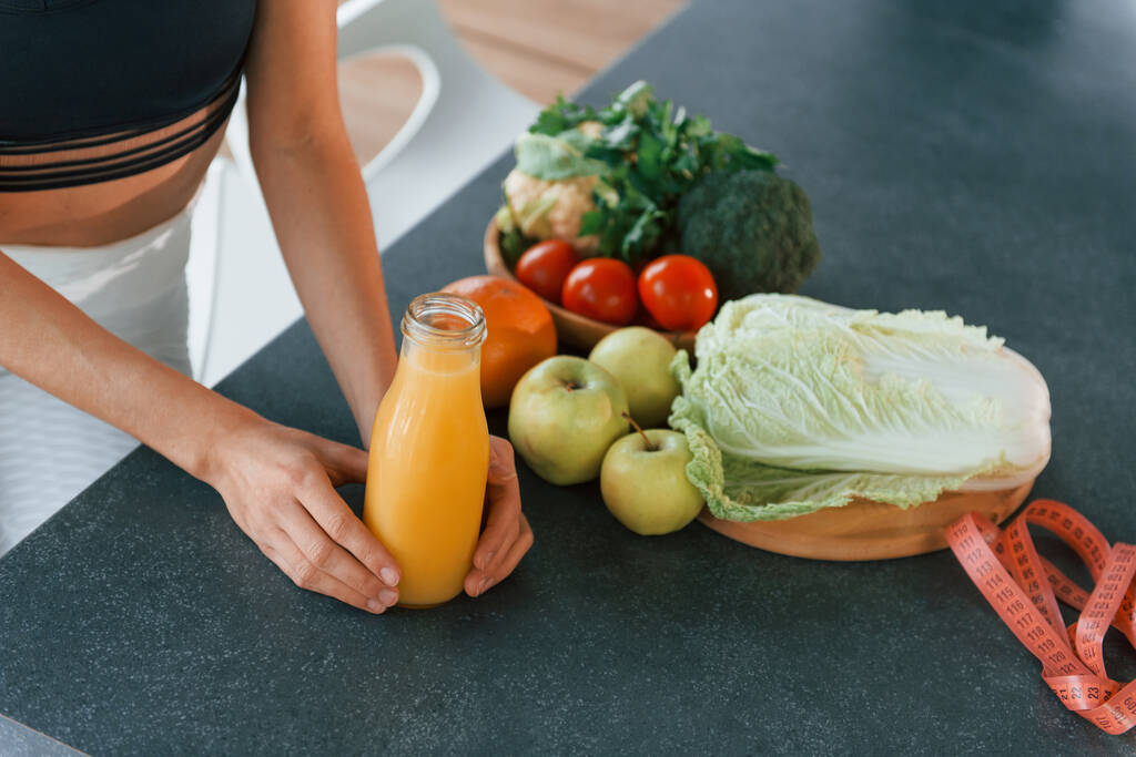 With fresh orange juice. Young european woman is indoors at kitchen indoors with healthy food. - Foto, Bild