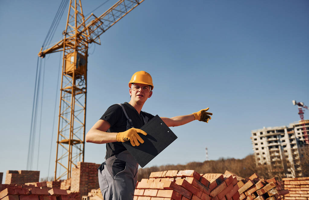 Ukazuje gesta a mluví. Stavební dělník v uniformě a bezpečnostním vybavení mají práci na stavbě. - Fotografie, Obrázek