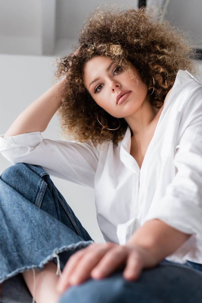 Low angle view of curly model in blouse looking at camera on white background  - Photo, Image