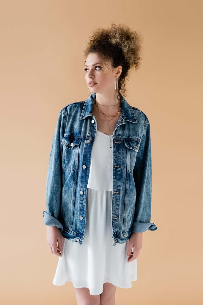 Smiling model in denim jacket looking away isolated on beige  - Photo, Image
