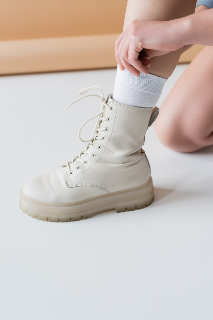 Cropped view of woman in boot adjusting sock on beige background - Photo, Image