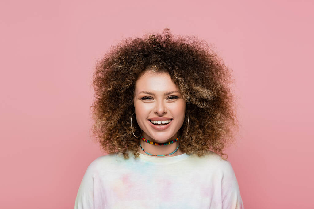 Cheerful curly woman looking at camera isolated on pink  - Photo, Image