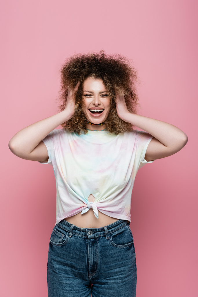 Onnellinen kihara nainen koskettaa hiukset eristetty vaaleanpunainen  - Valokuva, kuva