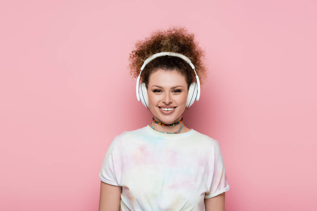 Mujer sonriente en camiseta y auriculares aislados en rosa  - Foto, imagen