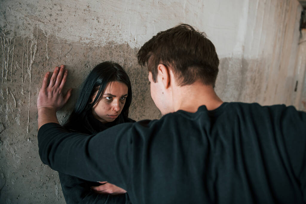 Kaçırılan kadın duvarın yanında duruyor ve terk edilmiş binadaki adam tarafından tehdit ediliyor.. - Fotoğraf, Görsel
