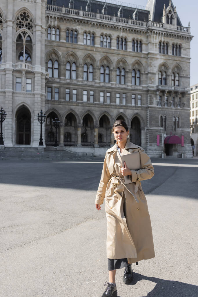Freelancer elegante em casaco de trincheira bege andando com laptop na rua de Viena  - Foto, Imagem