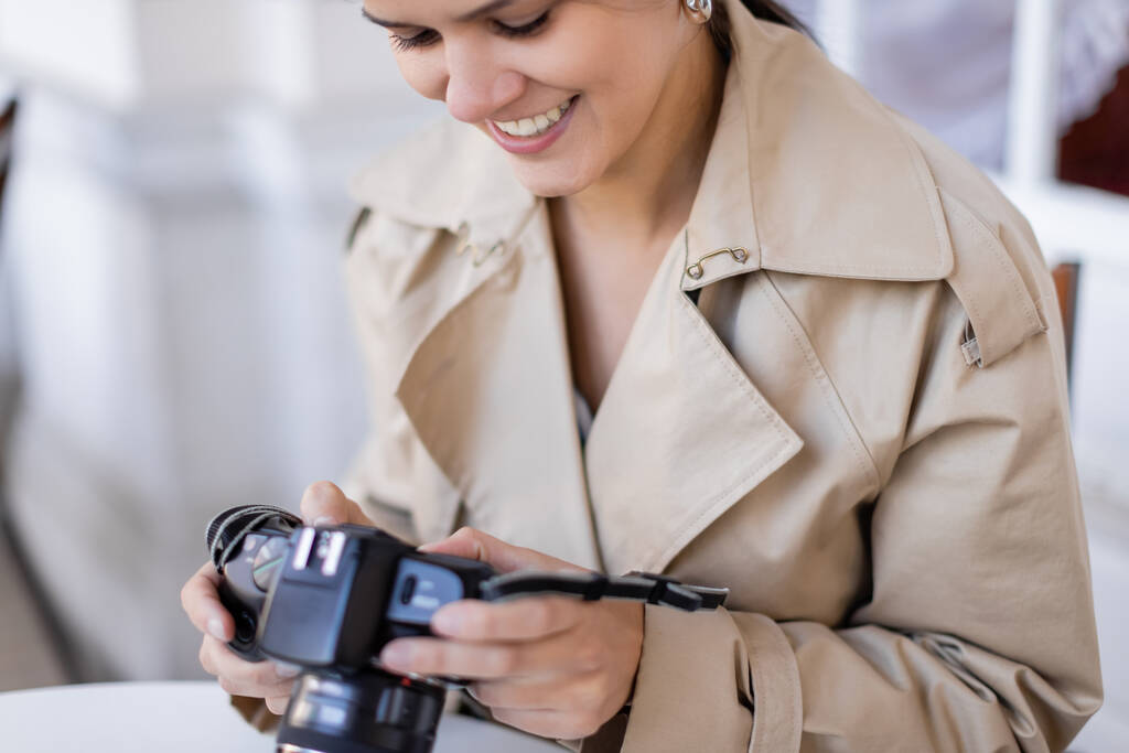 szczęśliwy fotograf w płaszczu okopowym patrząc na aparat cyfrowy  - Zdjęcie, obraz