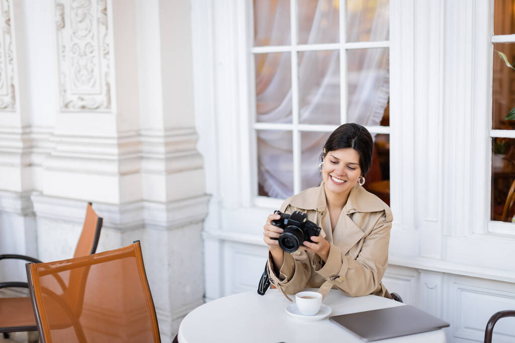 onnellinen valokuvaaja trenssi takki katsomalla digitaalikameraa  - Valokuva, kuva