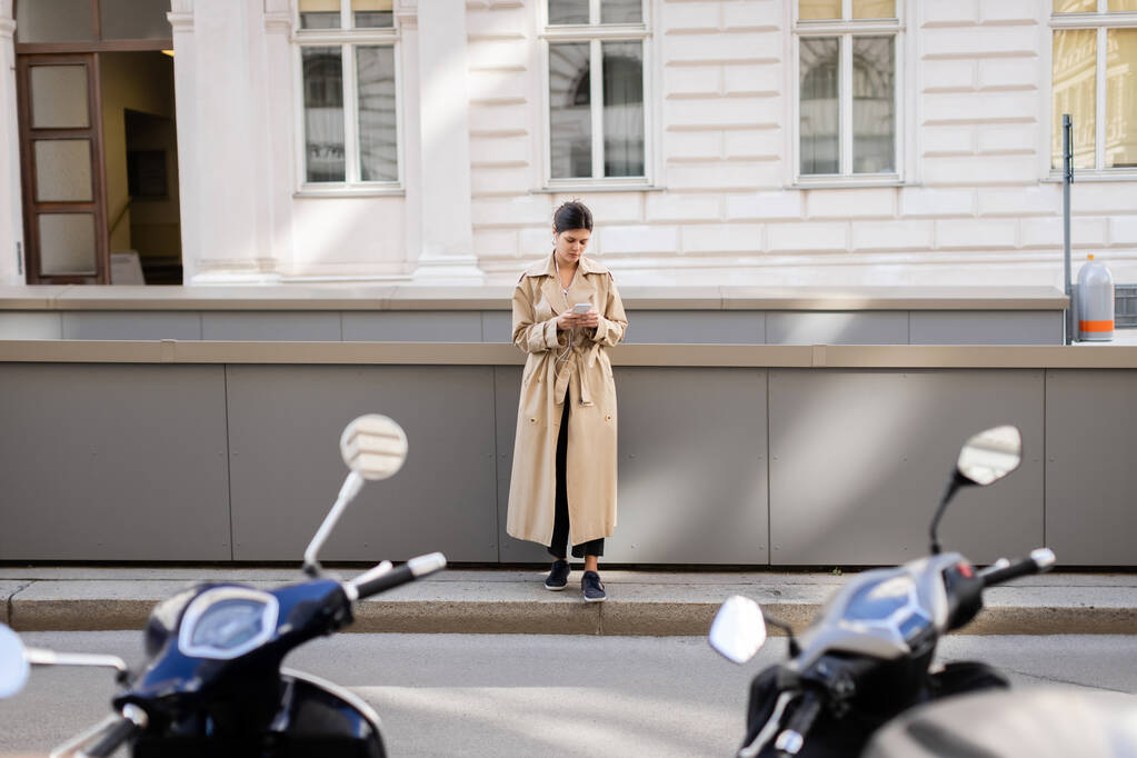 πλήρες μήκος της γυναίκας σε ενσύρματα ακουστικά κρατώντας κινητό τηλέφωνο και ακούγοντας μουσική στο δρόμο στη Βιέννη - Φωτογραφία, εικόνα