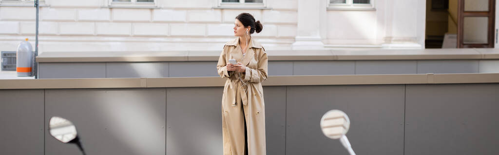 donna in cuffia cablata che tiene il cellulare e ascolta musica per strada a Vienna, banner - Foto, immagini