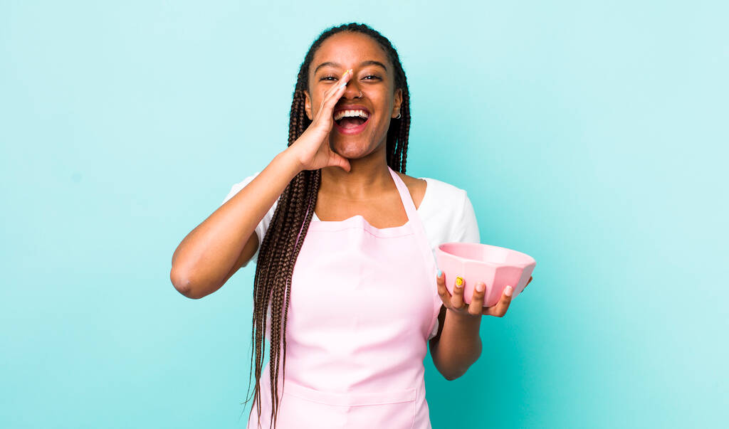 young adult black woman feeling happy,giving a big shout out with hands next to mouth. empty bowl concept - Foto, Imagem