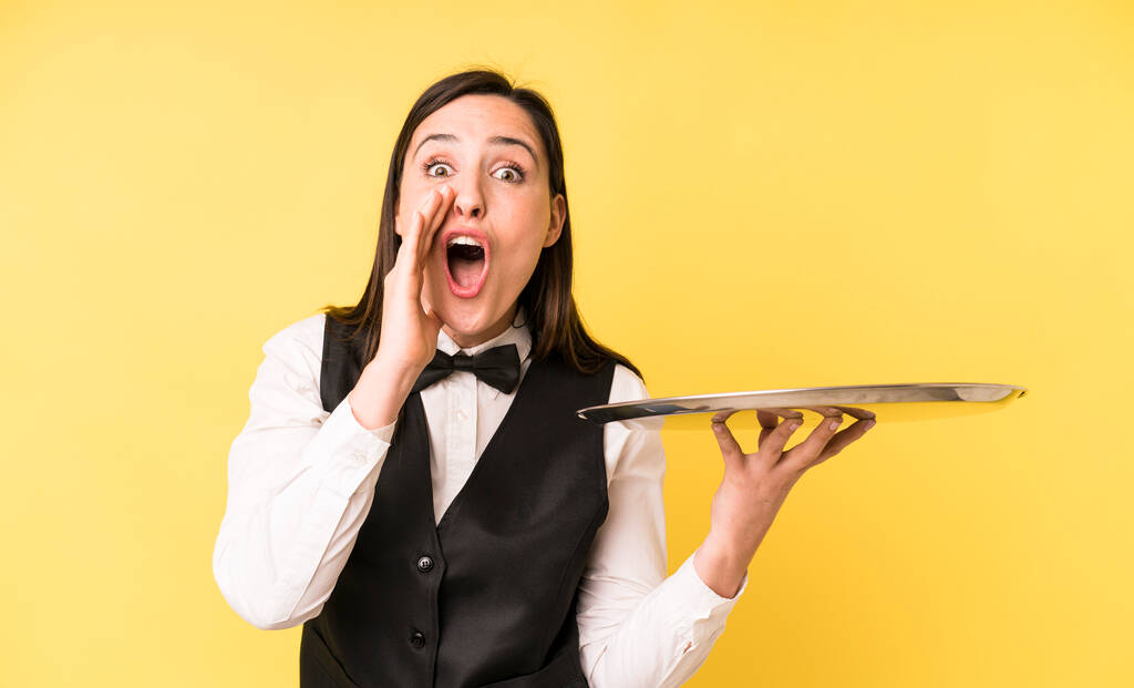 young adult pretty woman feeling happy,giving a big shout out with hands next to mouth. waiter and tray concept - Foto, imagen