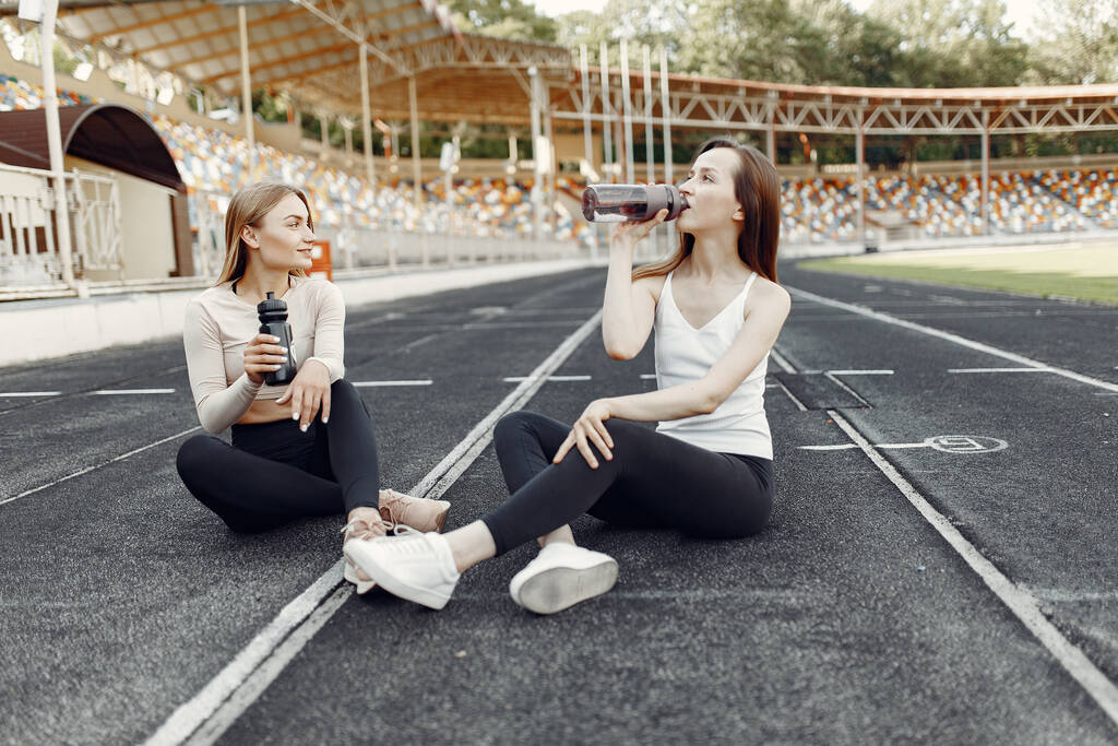 Спортивные девушки в форме сидят на стадионе - Фото, изображение