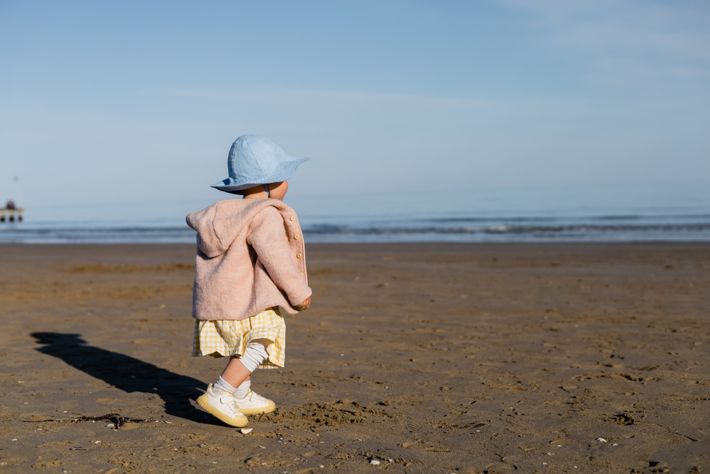 Baby girl in jacket and panama hat walking on beach in Italy  - Photo, Image