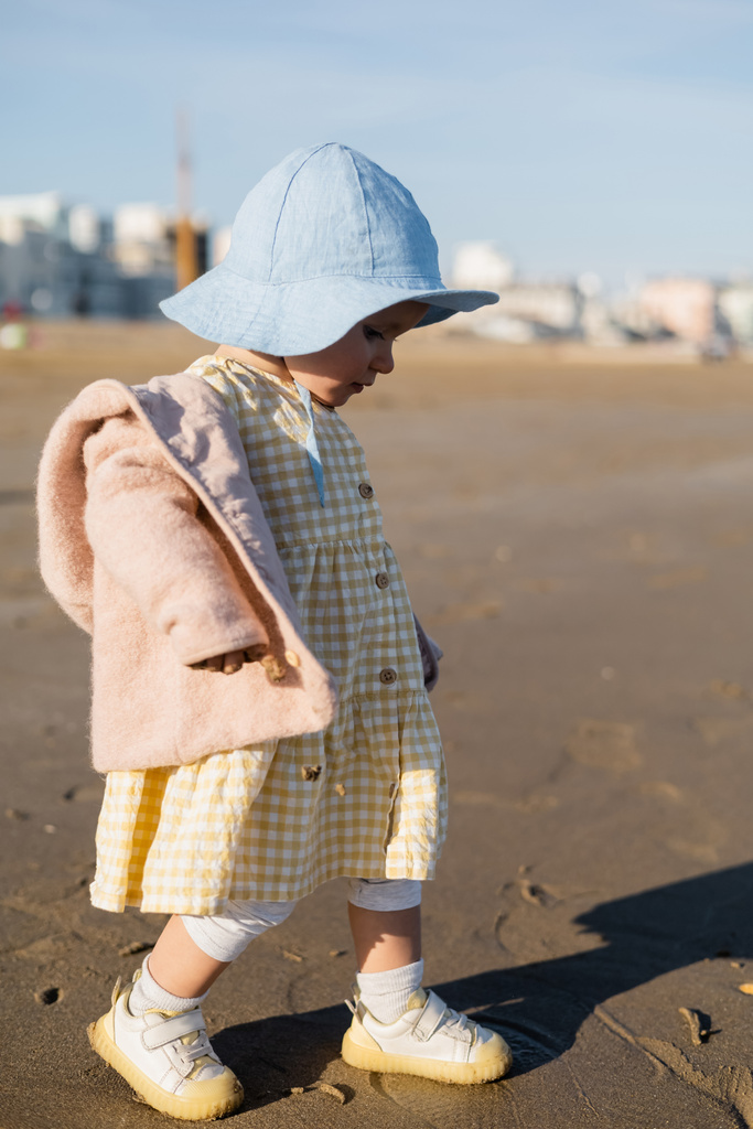 Вид збоку дівчинки в панамському капелюсі, що йде на піщаному пляжі
  - Фото, зображення
