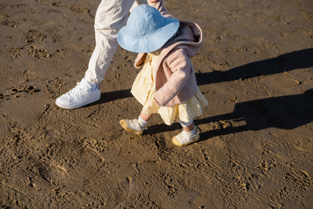 Высокий угол обзора маленькой девочки в панамской шляпе, идущей рядом с папой на пляже  - Фото, изображение