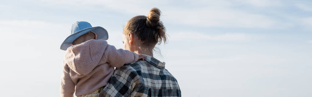 Νεαρός άνδρας κρατά το μωρό με μπλε ουρανό στο βάθος, λάβαρο  - Φωτογραφία, εικόνα