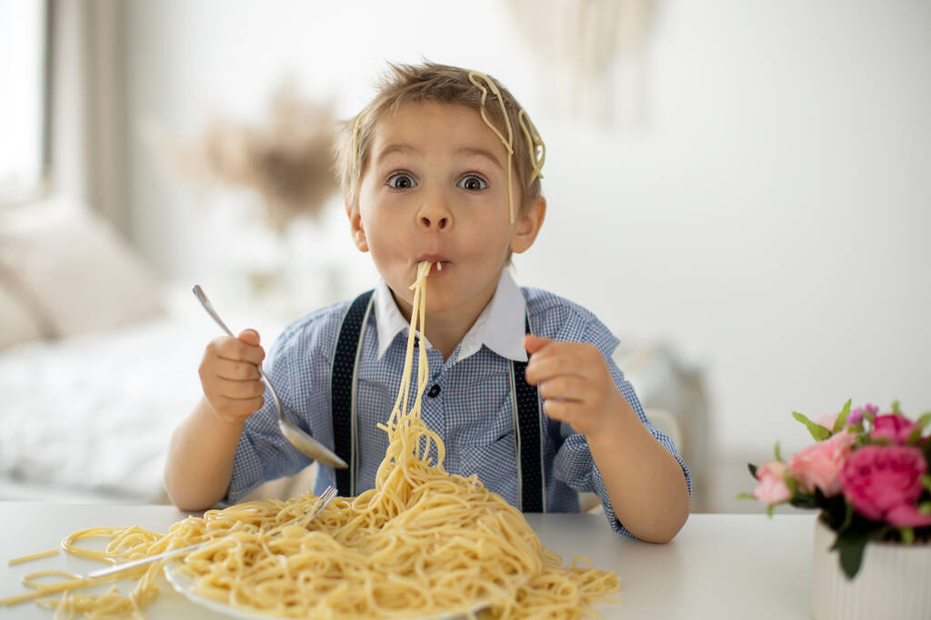 Милый ребенок в детском саду, блондин, ест спагетти дома, делает беспорядок везде, смешные моменты - Фото, изображение