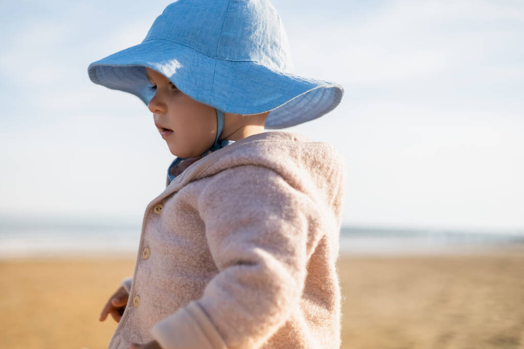 Niña en sombrero de panama de pie en la playa borrosa  - Foto, imagen