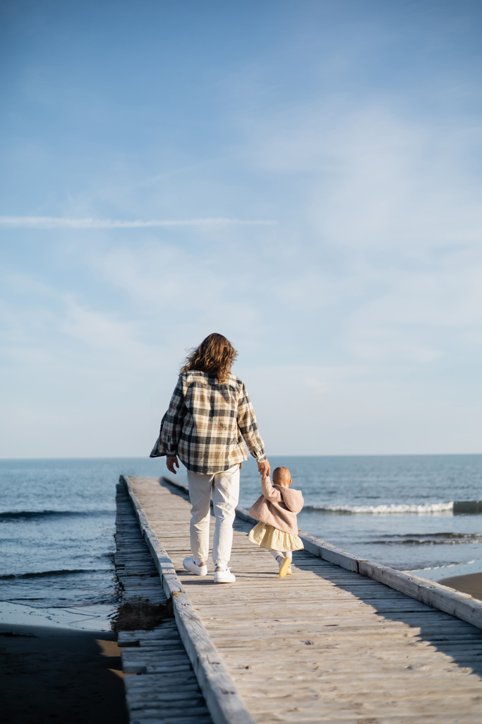 イタリアのアドリア海の近くの桟橋を歩く父と赤ちゃんの女の子のバックビュー  - 写真・画像
