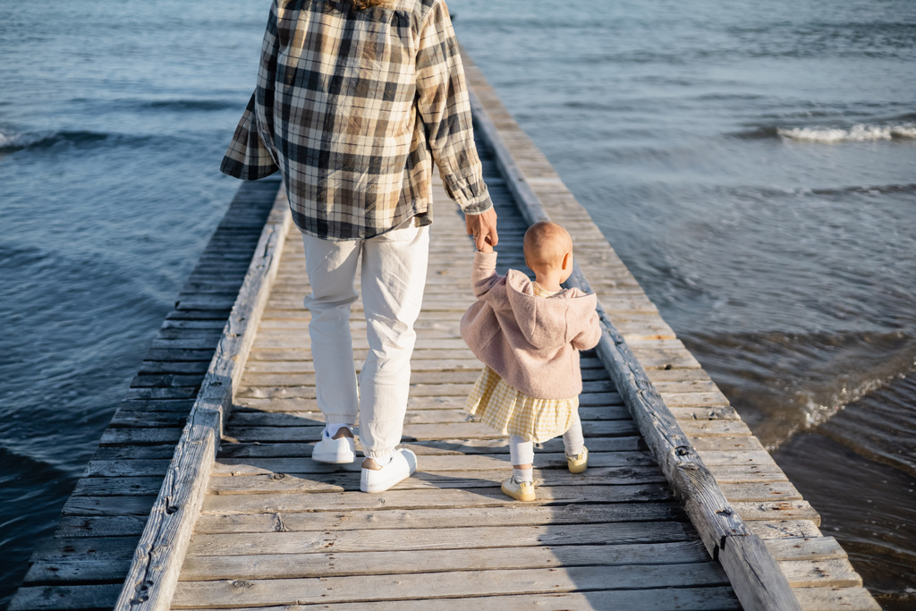 Pohled zezadu rodiče a holčička kráčející po dřevěném molu nad adriatickým mořem v Trevisu - Fotografie, Obrázek